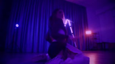 Baştan çıkarıcı dans eden seksi kadın. Titreyen bir dansçı, canlı mor ve mavi ışıkla yıkanmış, canlı neon bir üçgenin altında sahnenin enerjisini somutlaştırıyor. Bir sanatçının kadın vücudu, twerk ve yüksek topuklu ayakkabı sanatının bir kanıtı.