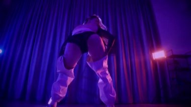 Baştan çıkarıcı dans eden seksi kadın. Titreyen bir dansçı, canlı mor ve mavi ışıkla yıkanmış, canlı neon bir üçgenin altında sahnenin enerjisini somutlaştırıyor. Bir sanatçının kadın vücudu, twerk ve yüksek topuklu ayakkabı sanatının bir kanıtı.