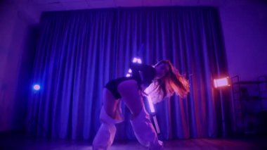 Baştan çıkarıcı dans eden seksi kadın. Titreyen bir dansçı, canlı mor ve mavi ışıkla yıkanmış, canlı neon bir üçgenin altında sahnenin enerjisini somutlaştırıyor. Bir sanatçının kadın vücudu, twerk ve yüksek topuklu ayakkabı sanatının bir kanıtı.