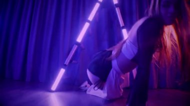 Baştan çıkarıcı dans eden seksi kadın. Titreyen bir dansçı, canlı mor ve mavi ışıkla yıkanmış, canlı neon bir üçgenin altında sahnenin enerjisini somutlaştırıyor. Bir sanatçının kadın vücudu, twerk ve yüksek topuklu ayakkabı sanatının bir kanıtı.