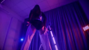 Baştan çıkarıcı dans eden seksi kadın. Titreyen bir dansçı, canlı mor ve mavi ışıkla yıkanmış, canlı neon bir üçgenin altında sahnenin enerjisini somutlaştırıyor. Bir sanatçının kadın vücudu, twerk ve yüksek topuklu ayakkabı sanatının bir kanıtı.
