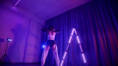 Baştan çıkarıcı dans eden seksi kadın. Titreyen bir dansçı, canlı mor ve mavi ışıkla yıkanmış, canlı neon bir üçgenin altında sahnenin enerjisini somutlaştırıyor. Bir sanatçının kadın vücudu, twerk ve yüksek topuklu ayakkabı sanatının bir kanıtı.