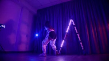 Baştan çıkarıcı dans eden seksi kadın. Titreyen bir dansçı, canlı mor ve mavi ışıkla yıkanmış, canlı neon bir üçgenin altında sahnenin enerjisini somutlaştırıyor. Bir sanatçının kadın vücudu, twerk ve yüksek topuklu ayakkabı sanatının bir kanıtı.