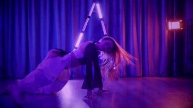 Baştan çıkarıcı dans eden seksi kadın. Titreyen bir dansçı, canlı mor ve mavi ışıkla yıkanmış, canlı neon bir üçgenin altında sahnenin enerjisini somutlaştırıyor. Bir sanatçının kadın vücudu, twerk ve yüksek topuklu ayakkabı sanatının bir kanıtı.
