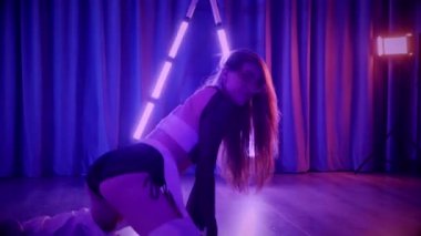 Baştan çıkarıcı dans eden seksi kadın. Titreyen bir dansçı, canlı mor ve mavi ışıkla yıkanmış, canlı neon bir üçgenin altında sahnenin enerjisini somutlaştırıyor. Bir sanatçının kadın vücudu, twerk ve yüksek topuklu ayakkabı sanatının bir kanıtı.