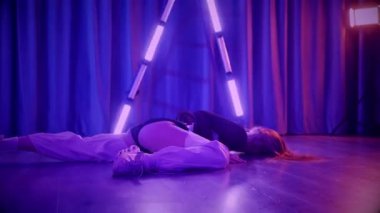 Baştan çıkarıcı dans eden seksi kadın. Titreyen bir dansçı, canlı mor ve mavi ışıkla yıkanmış, canlı neon bir üçgenin altında sahnenin enerjisini somutlaştırıyor. Bir sanatçının kadın vücudu, twerk ve yüksek topuklu ayakkabı sanatının bir kanıtı.