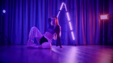 Baştan çıkarıcı dans eden seksi kadın. Titreyen bir dansçı, canlı mor ve mavi ışıkla yıkanmış, canlı neon bir üçgenin altında sahnenin enerjisini somutlaştırıyor. Bir sanatçının kadın vücudu, twerk ve yüksek topuklu ayakkabı sanatının bir kanıtı.