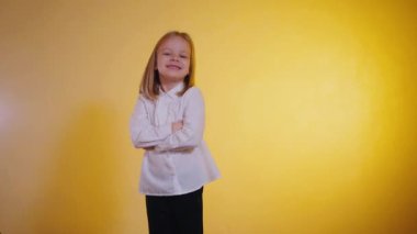 Işıl ışıl genç bir kız, kolları çapraz, sıcak, altın bir zemin üzerinde ışıl ışıl gülümsüyor. Kendine güvenen ve çekici, beyaz gömlekli ve siyah pantolonlu küçük bir kız, parlak sarı bir arka plana karşı poz veriyor. Neşeli bir çocuk, pozitif ışıldıyor,