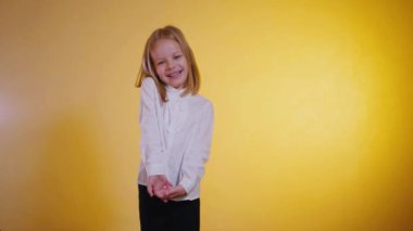 Işıl ışıl genç bir kız utangaç ve ışıl ışıl gülümser sıcak, altın bir arkaplana karşı. Kendine güvenen, çekici, beyaz gömlekli ve siyah pantolonlu küçük bir kız. 