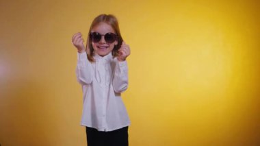 Kendine güveni olan genç bir kız, sanki para topluyormuş gibi elleriyle bir jest yapıyor. Bir çocuğun neşeli ifadesi, parlak sarı bir arka plana karşı ellerini birbirine sürterek. Bir altın parıltısı, biraz zenginlik ve bir çocuğun neşeli ifadesi.. 