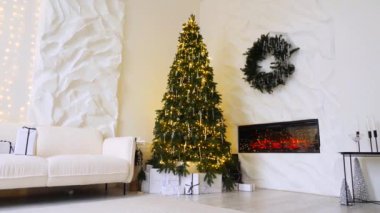 Noel ışıklarının parıltısı, görkemli bir ağaç ve sıcak bir şömineyle tamamlanmış sofistike bir oturma odasını aydınlatır. Modern bir evde, bir Noel ağacı, bir şömine ve yumuşak, davetkar bir atmosfere sahip bir kış harikalar diyarı.