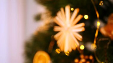 Sıcak, altın ışıklar ve el yapımı süslemelerle süslenmiş Noel ağacı. Noel ağacı dalları, parlak ışıklar, ve el yapımı saman yıldızı, turuncu, sıcak ve davetkar bir atmosfer yaratıyor. Peri ışıklarının yumuşak parıltısı aydınlatır