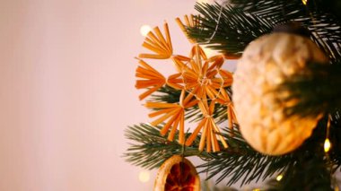 Sıcak, altın ışıklar ve el yapımı süslemelerle süslenmiş Noel ağacı. Noel ağacı dalları, parlak ışıklar, ve el yapımı saman yıldızı, turuncu, sıcak ve davetkar bir atmosfer yaratıyor. Peri ışıklarının yumuşak parıltısı aydınlatır