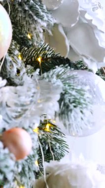 Dikey, Noel ağacı dalları, narin bir kar yağışı ile süslenmiş, zarif süsler sergiliyor. Süslü bir Noel ağacının yakın çekimi. Zarif süsler ve parıldayan ışıklar sergiliyor..