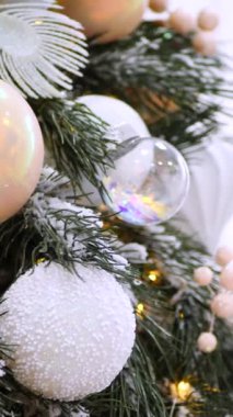 Dikey, Noel ağacı dalları, narin bir kar yağışı ile süslenmiş, zarif süsler sergiliyor. Süslü bir Noel ağacının yakın çekimi. Zarif süsler ve parıldayan ışıklar sergiliyor..