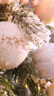 Dikey, Noel ağacı dalları, narin bir kar yağışı ile süslenmiş, zarif süsler sergiliyor. Süslü bir Noel ağacının yakın çekimi. Zarif süsler ve parıldayan ışıklar sergiliyor..