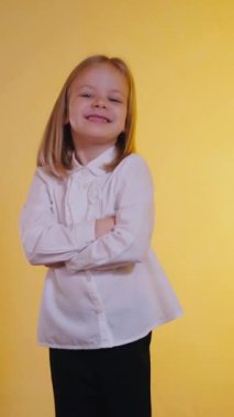 Işıl ışıl genç bir kız, kolları çapraz, sıcak, altın bir zemin üzerinde ışıl ışıl gülümsüyor. Kendine güvenen ve çekici, beyaz gömlekli ve siyah pantolonlu küçük bir kız, canlı sarı bir kıza karşı poz veriyor.