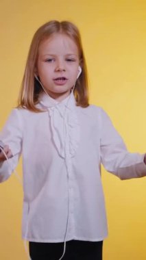 Dikey, enerjik mutlu kız, kulaklıklar takılı, ritimle dans ediyor ve gülüyor. Canlı sarı bir fon, beyazlı küçük bir kız telefonda müzik dinliyor ve mutlu bir şekilde şarkı söylüyor.