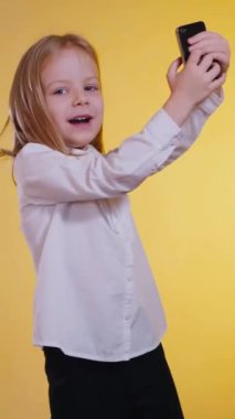 Dikey olarak, çocuk telefonda görüntülü konuşma yaparken eğleniyor. Selfie Mutlu Çocuk güneş gözlüğü takıyor, aferin. Gülümseyen kız başparmağını kaldırıyor. Olumlu jestli kadın.