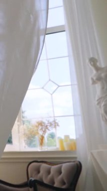 Dikey, parlak odada dalgalı beyaz perdeler var. Narin kuş kafesi ve dalgalı beyaz perdeleri olan sakin bir oda. Beyaz şeffaf kumaş rüzgarda dalgalanıyor. Parlak bir stüdyoda uzun beyaz perdeler