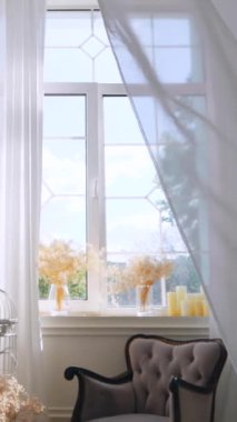 Dikey, parlak odada dalgalı beyaz perdeler var. Narin kuş kafesi ve dalgalı beyaz perdeleri olan sakin bir oda. Beyaz şeffaf kumaş rüzgarda dalgalanıyor. Parlak bir stüdyoda uzun beyaz perdeler