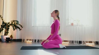 Yoga yaparken güneşli bir odada esneyen pembe elbiseli bir kadın. Gülümseyen kadın esneme egzersizleri yapar. Esneklik eğitimi, esneklik hareketleri, fiziksel egzersizler. Esneme sanatı, dinamik yoga pozu veren bir kadın. Esniyorum.