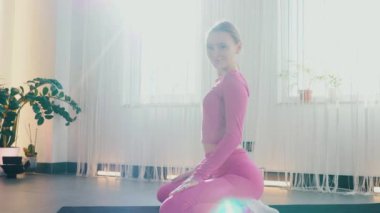 Yoga yaparken güneşli bir odada esneyen pembe elbiseli bir kadın. Gülümseyen kadın esneme egzersizleri yapar. Esneklik eğitimi, esneklik hareketleri, fiziksel egzersizler. Esneme sanatı, dinamik yoga pozu veren bir kadın. Esniyorum.