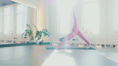 Yoga yaparken güneşli bir odada esneyen pembe elbiseli bir kadın. Gülümseyen kadın esneme egzersizleri yapar. Esneklik eğitimi, esneklik hareketleri, fiziksel egzersizler. Esneme sanatı, dinamik yoga pozu veren bir kadın. Esniyorum.