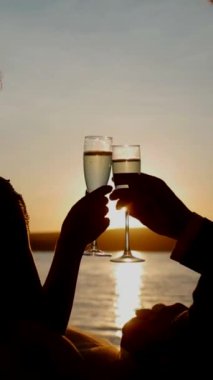 Dikey. Birbirine aşık bir çift şampanya bardaklarını tutar ve gün batımında nehir kıyısında durur. Gelin ve damat el ele tutuşuyor. Öpüşen aşıkların siluetleri.