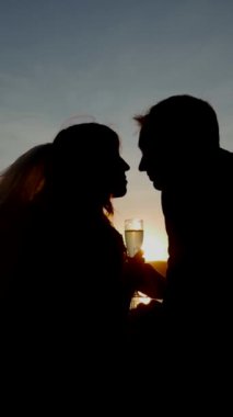 Dikey. Birbirine aşık bir çift şampanya bardaklarını tutar ve gün batımında nehir kıyısında durur. Gelin ve damat el ele tutuşuyor. Öpüşen aşıkların siluetleri.