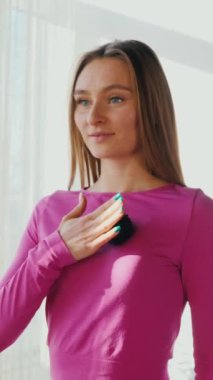 Dikey. Gülümseyen kadın esneme egzersizleri yapar. Yoga yaparken güneşli bir odada esneyen pembe elbiseli bir kadın. Esneklik eğitimi, fiziksel egzersizler.