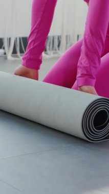 Dikey. Gülümseyen kadın esneme egzersizleri yapar. Yoga yaparken güneşli bir odada esneyen pembe elbiseli bir kadın. Esneklik eğitimi, fiziksel egzersizler.