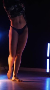Vertical, Sexy woman dancing a seductive dance. A dancer girl with a big ass in a thong dances erotically in a dark hall. Twerk, high heels, striptease