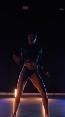 Vertical, Sexy woman dancing a seductive dance. A dancer girl with a big ass in a thong dances erotically in a dark hall. Twerk, high heels, striptease