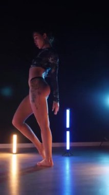 Vertical, Sexy woman dancing a seductive dance. A dancer girl with a big ass in a thong dances erotically in a dark hall. Twerk, high heels, striptease