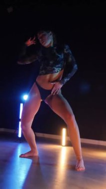 Vertical, Sexy woman dancing a seductive dance. A dancer girl with a big ass in a thong dances erotically in a dark hall. Twerk, high heels, striptease