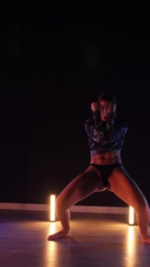 Vertical, Sexy woman dancing a seductive dance. A dancer girl with a big ass in a thong dances erotically in a dark hall. Twerk, high heels, striptease