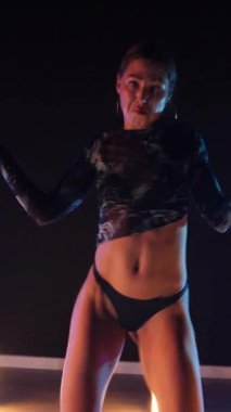 Vertical, Sexy woman dancing a seductive dance. A dancer girl with a big ass in a thong dances erotically in a dark hall. Twerk, high heels, striptease