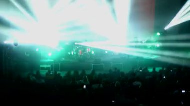 Canlı performans enerjisiyle dolu canlı bir konser salonu. Canlı bir ışık ve ses gösterisi, kalabalığı büyülüyor. Sahnede bir rock grubu çalıyor. Bando sahneyi ateşlerken elektrik enerjisi mekanı dolduruyor..