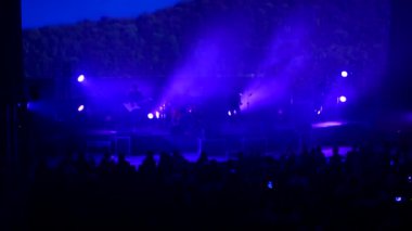 Canlı performans enerjisiyle dolu canlı bir konser salonu. Canlı bir ışık ve ses gösterisi, kalabalığı büyülüyor. Sahnede bir rock grubu çalıyor. Bando sahneyi ateşlerken elektrik enerjisi mekanı dolduruyor..