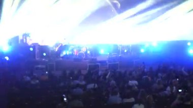 Canlı performans enerjisiyle dolu canlı bir konser salonu. Canlı bir ışık ve ses gösterisi, kalabalığı büyülüyor. Sahnede bir rock grubu çalıyor. Bando sahneyi ateşlerken elektrik enerjisi mekanı dolduruyor..