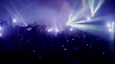 Canlı performans enerjisiyle dolu canlı bir konser salonu. Canlı bir ışık ve ses gösterisi, kalabalığı büyülüyor. Sahnede bir rock grubu çalıyor. Bando sahneyi ateşlerken elektrik enerjisi mekanı dolduruyor..