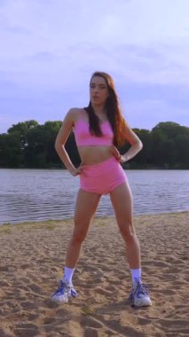 Sahilde dans eden dikey, seksi kız. Güzel bir kadın kalçasıyla kumda dans eder. Bikinili seksi kadın. Bikinili genç bir kadın kumların üzerinde enerjik bir dans ediyor..