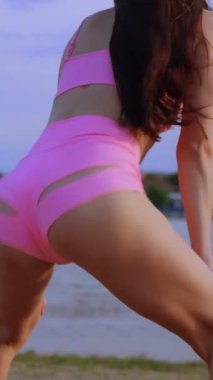 Sahilde dans eden dikey, seksi kız. Güzel bir kadın kalçasıyla kumda dans eder. Bikinili seksi kadın. Bikinili genç bir kadın kumların üzerinde enerjik bir dans ediyor..