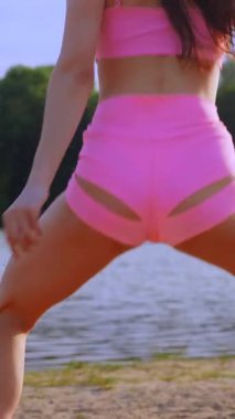 Sahilde dans eden dikey, seksi kız. Güzel bir kadın kalçasıyla kumda dans eder. Bikinili seksi kadın. Bikinili genç bir kadın kumların üzerinde enerjik bir dans ediyor..