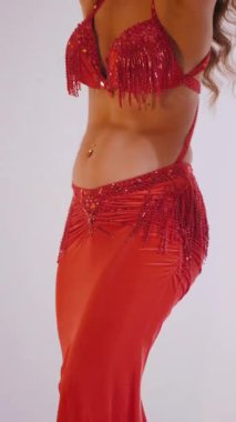 Dikey. Güzel kız oryantal göbek dansı yapıyor. Kırmızı iç çamaşırlı seksi kadın beyaz bir stüdyoda baştan çıkarıcı bir dans yapıyor. Yavaş çekim. Güzel karın ve göğüsler..