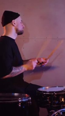Dikey. Stüdyoda bir adam davul çalıyor. Sürücü müzisyen davulcu soğukkanlılıkla davulda rock çalar. Stüdyo, renk arkaplanı.