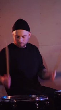 Dikey. Stüdyoda bir adam davul çalıyor. Sürücü müzisyen davulcu soğukkanlılıkla davulda rock çalar. Stüdyo, renk arkaplanı.
