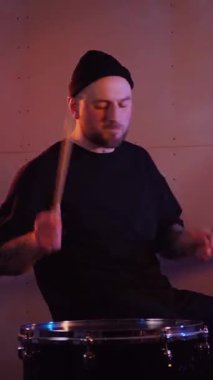 Dikey. Stüdyoda bir adam davul çalıyor. Sürücü müzisyen davulcu soğukkanlılıkla davulda rock çalar. Stüdyo, renk arkaplanı.