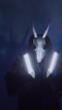 Dikey olarak şeytan elinde RGB çubuklarıyla dans ediyor. Karanlık bir stüdyoda maskeli gizemli bir adam. Adam siyah bir ceket ve boynuzlu bir maske giymiş. Uzaylı uzaylı. Korkunç.,